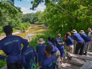 A group of teenagers wearing matching blue t-shirts, lined up along a wooden deck, overlooking a river in the summer.
